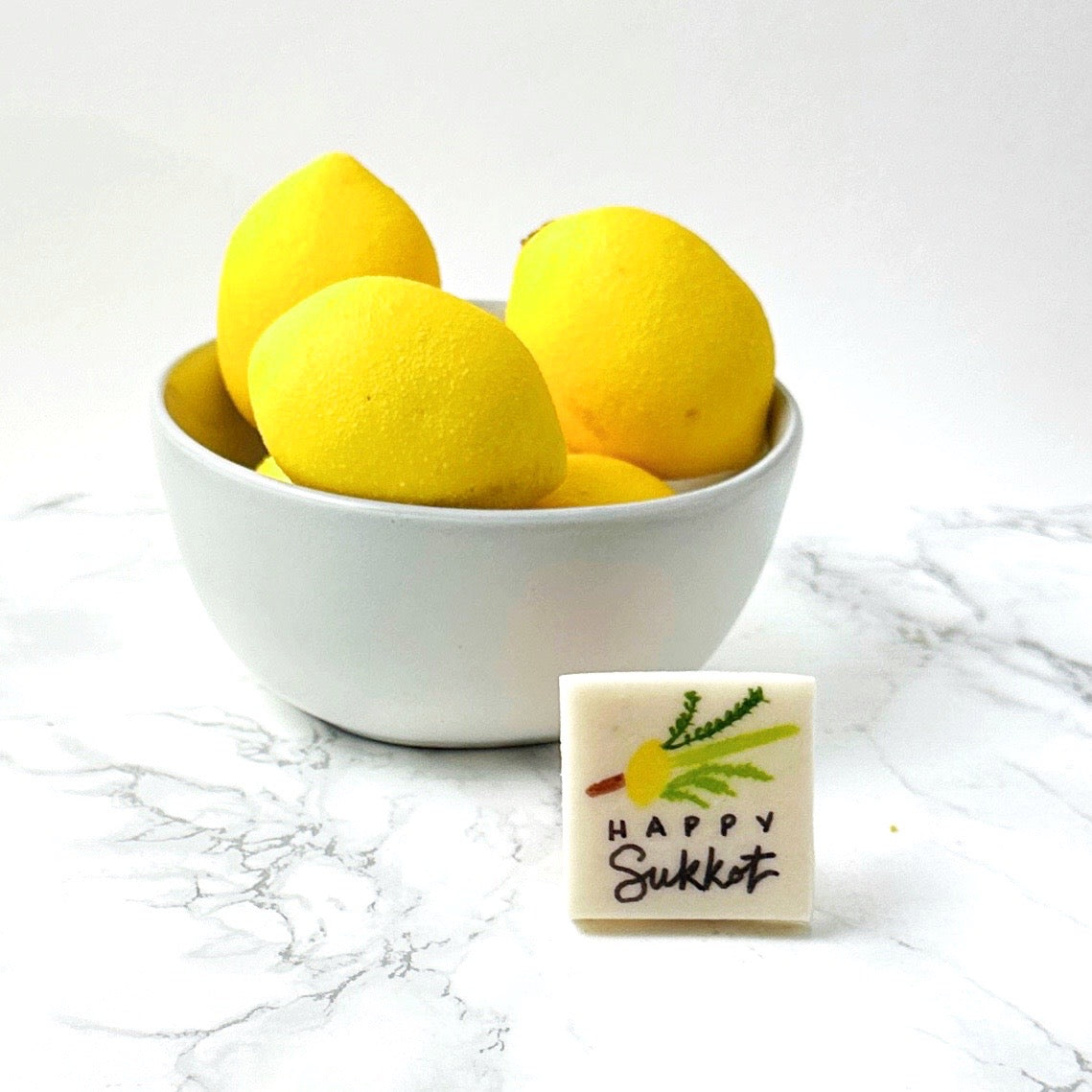 Happy Sukkot marzipan place card displayed beside a bowl of yellow citrus fruit