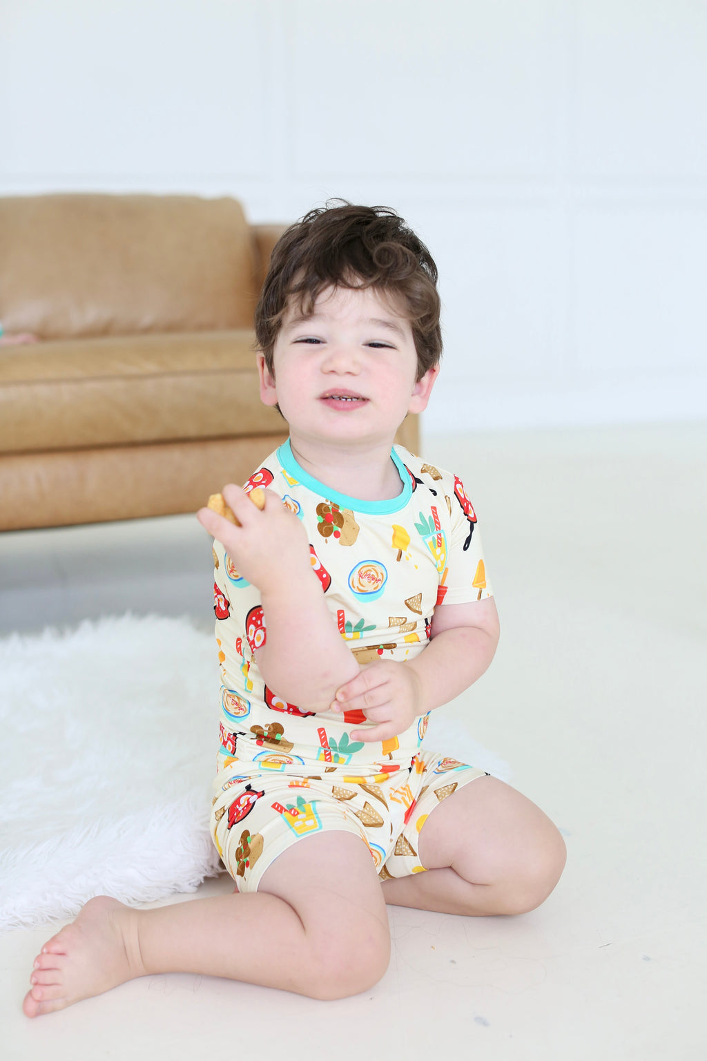 Child seated in the Taste of Israel short-sleeve pajama set featuring falafel, pita and hummus illustrations