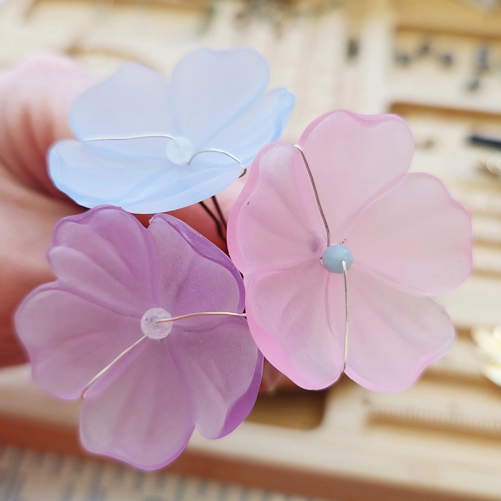 Light blue, lavender and baby pink lucite poppy hairpins held in hand
